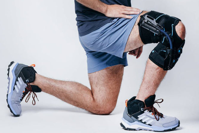 Person wearing a knee brace and athletic shoes on a plain background
